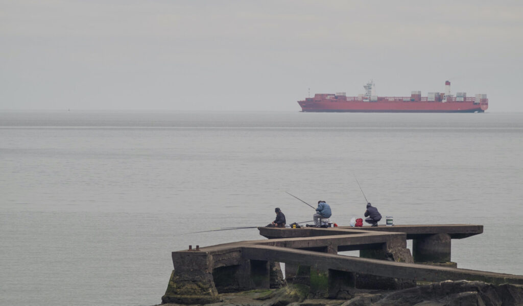 MONTEVIDEO, URUGUAY, JULY18, 2015: People fishing on Rio de la Plata while a large container ship sails by. Montevideo is on of